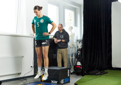 Physiotherapeut Malte Klett überwacht das Training einer Sportlerin die auf einer Vibrationsplatte schwebt - Sport & Schmerz Campus