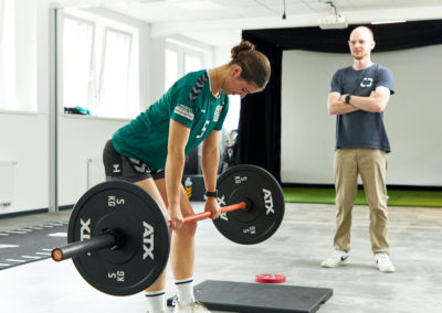Personal Trainer Malte Klett leitet Sportlerinan der Langhantel an in den Trainingsräumen des Sport & Schmerz Campus